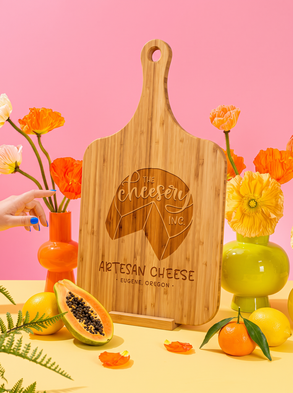 Custom logo engraved on a bamboo handle cutting board, styled with colorful flowers against a pink background.