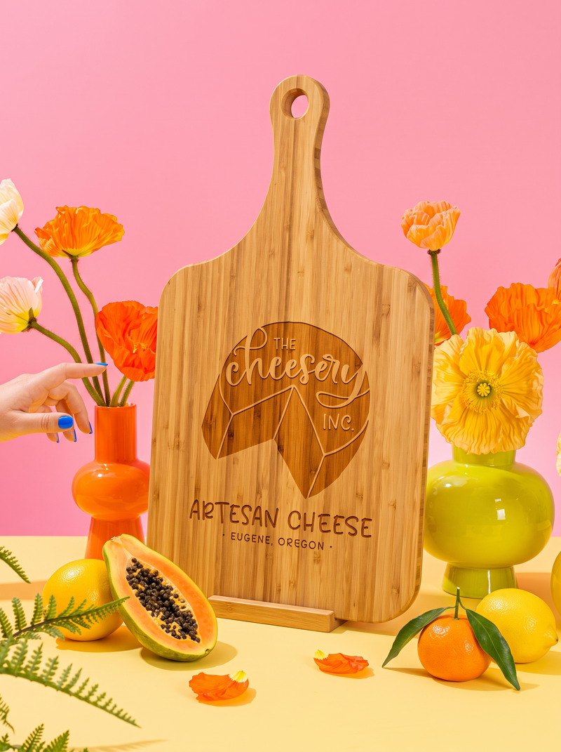 Custom logo engraved on a bamboo handle cutting board, styled with colorful flowers against a pink background.
