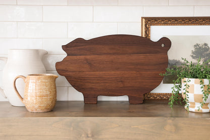 a wooden cutting board, a ceramic pitcher, a potted plant, and a framed picture on a wooden shelf.