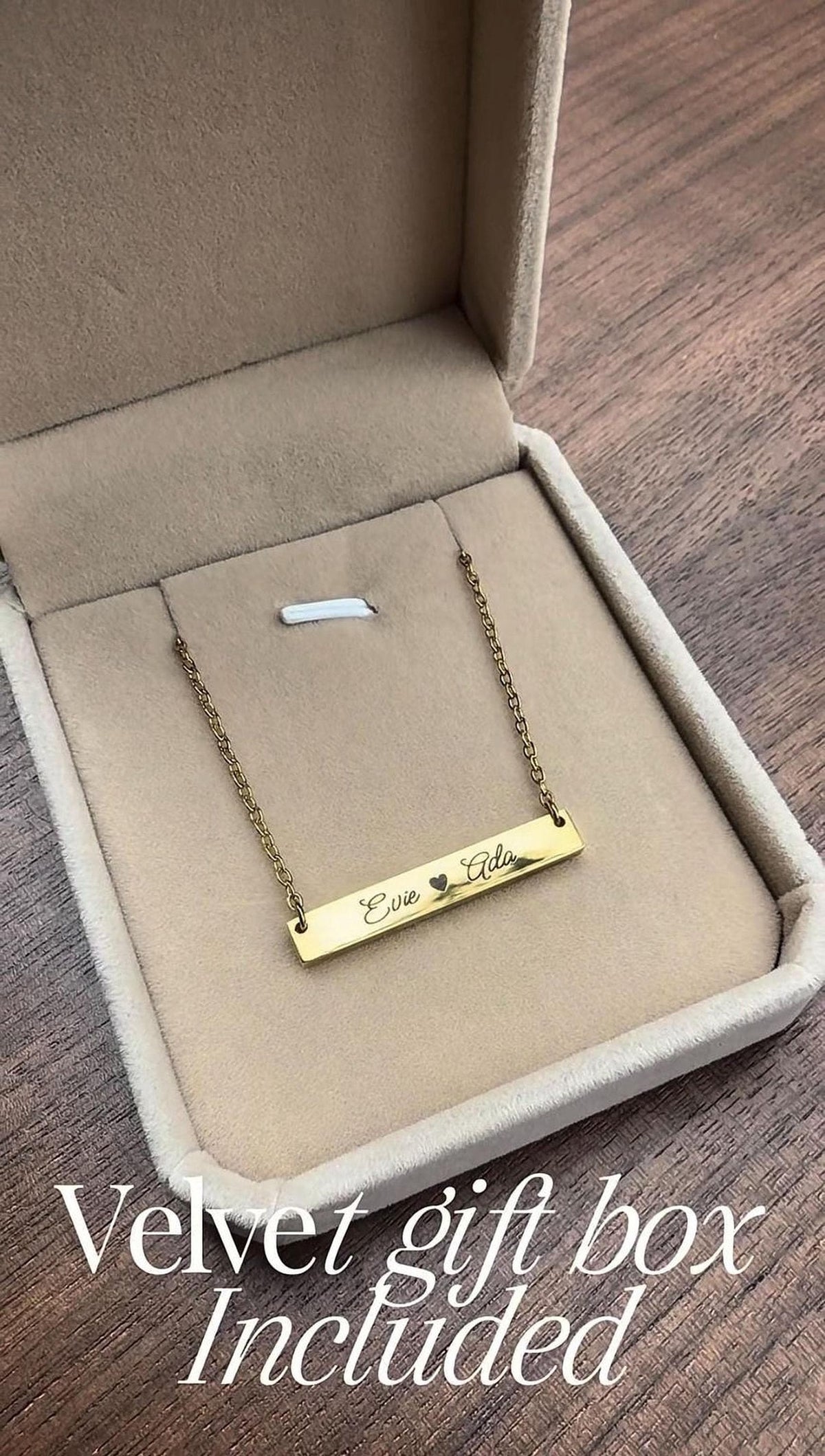 A gold-colored necklace with a personalized engraved bar is displayed in a velvet gift box, which is included as part of the gift.