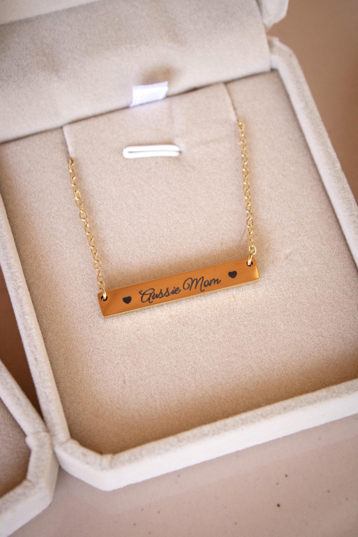 A gold necklace with a rectangular pendant engraved with the text "Closest Mom" is displayed in a white jewelry box.
