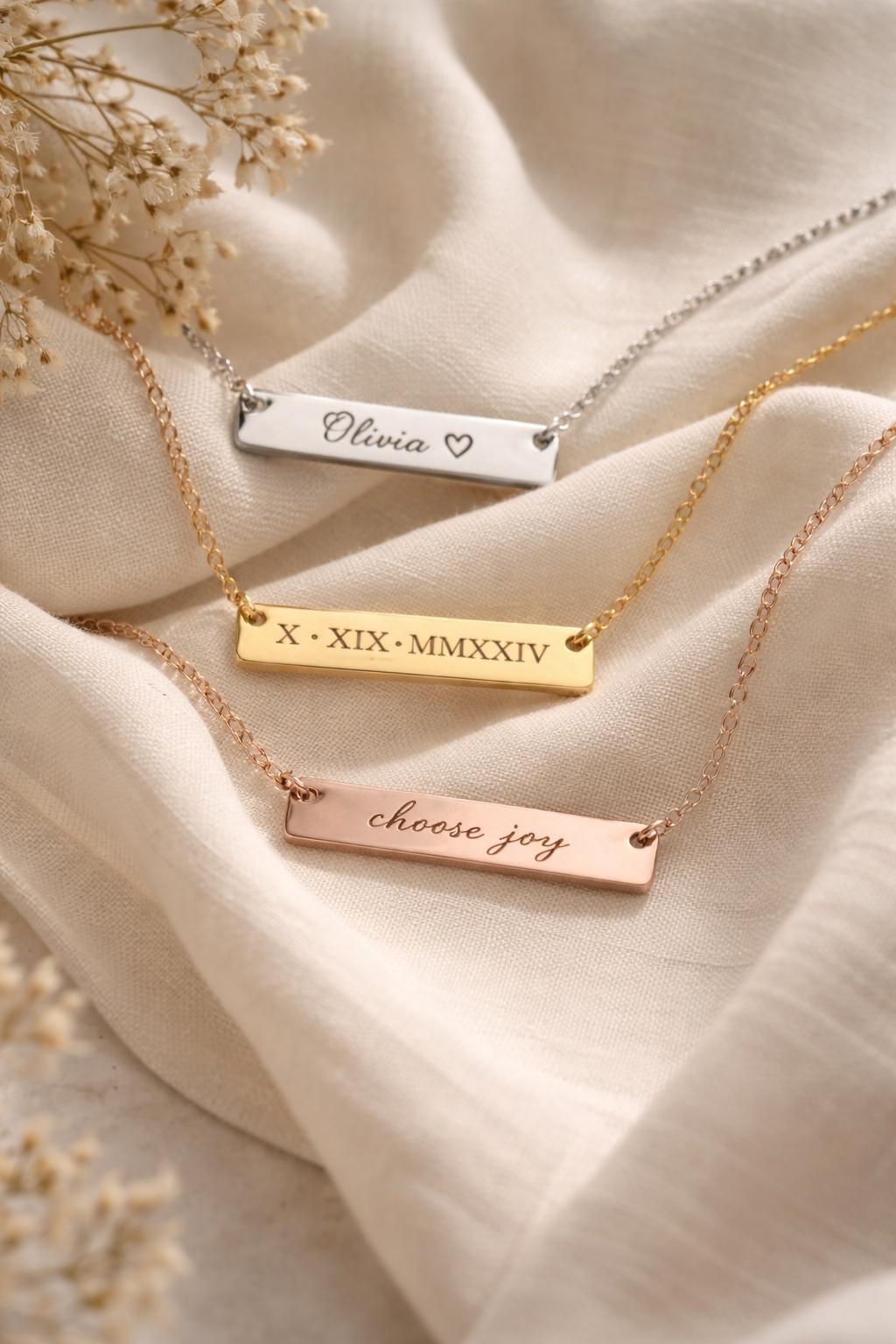 Three gold necklaces with engraved names and phrases on a beige fabric background.