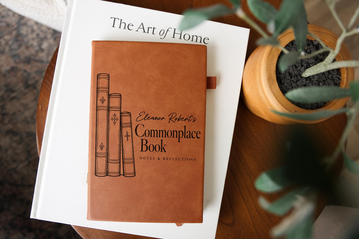 Edited mockup of a brown journal on a white book beside a potted plant; three vintage-style book spines and Eleanor Robert’s Commonplace Book, Notes & Reflections cover design.