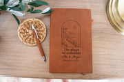 Places journal mockup with a chestnut-colored cover beside a pen and woven coaster; arched coastal artwork above The places we remember and sample names and date.