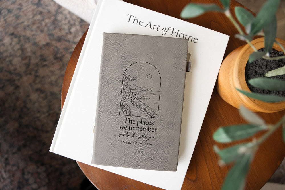 Places journal mockup with a gray cover on a white book beside a plant; coastal path artwork, The places we remember, Alex & Morgan and September 19, 2026.