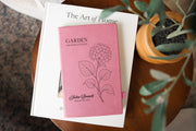 Pink Garden Hydrangea journal mockup on a book beside a potted plant. Cover shows a hydrangea, Garden Observations, Julia Bennett, and Field Notes.