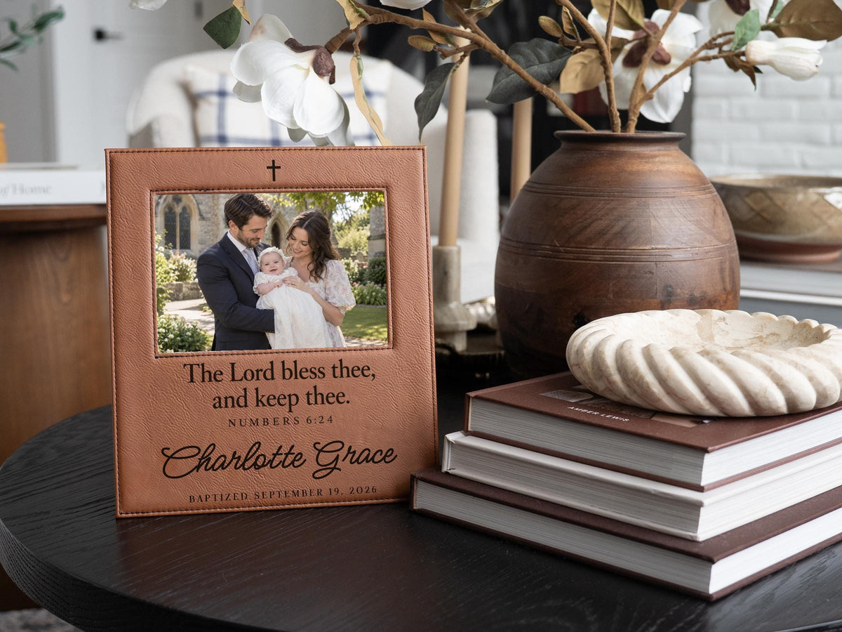 Edited mockup of the charlotte grace baptism frame beside books and flowers, with a cross, Numbers 6:24 blessing, sample name and date, and an illustrative family photograph.