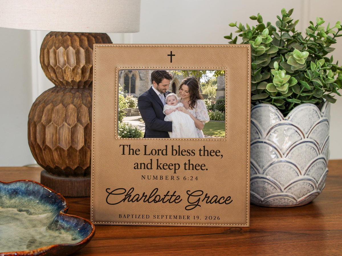 Edited mockup of the charlotte grace baptism frame beside a lamp and plant, with an illustrative family photograph, cross, Numbers 6:24 blessing, sample name and date.