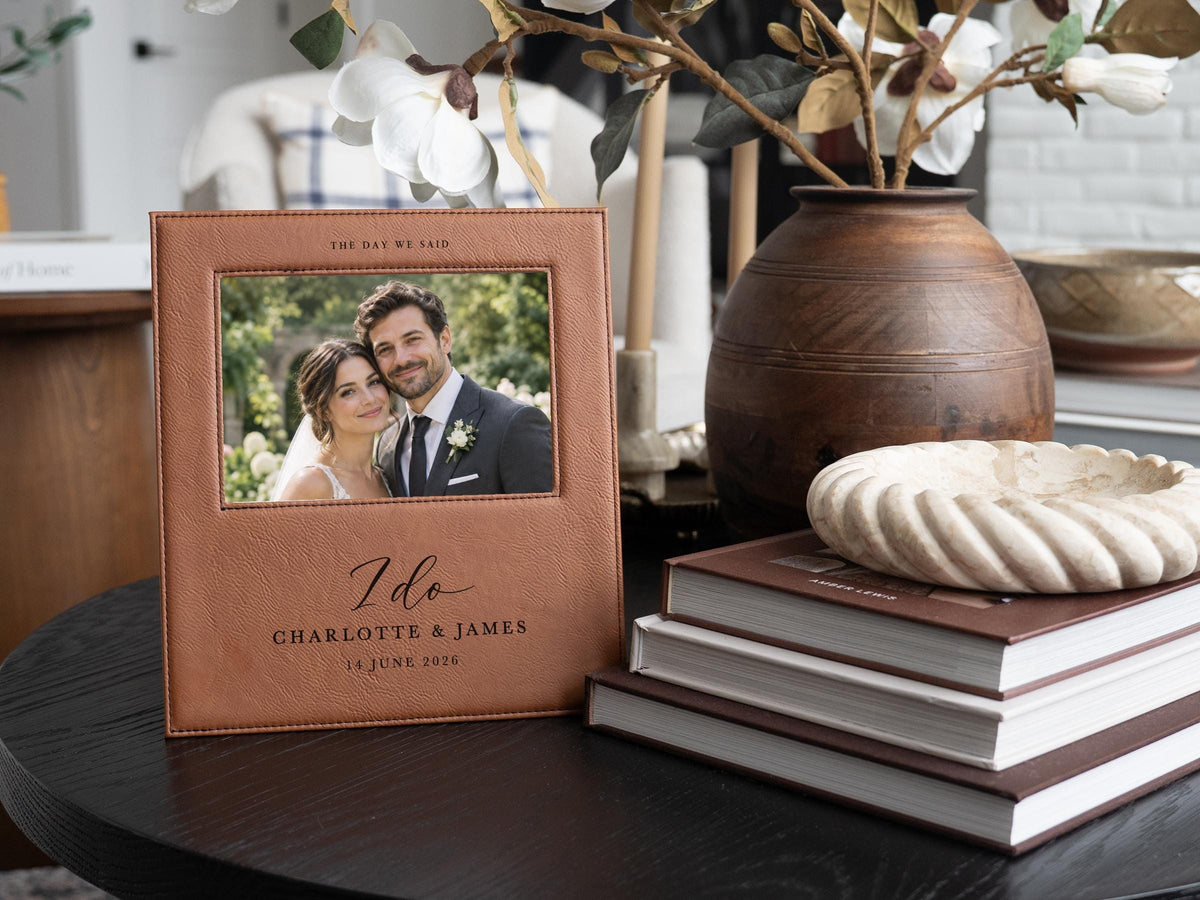 I Do wedding frame mockup beside books and a vase of white flowers, with an illustrative couple photo and the sample names Charlotte & James and date 14 June 2026.