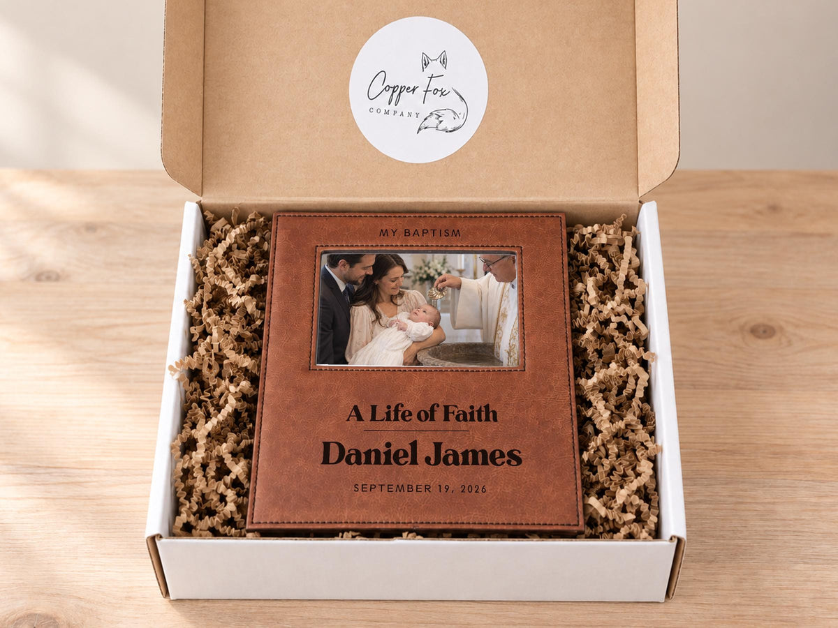 Edited mockup of the life of faith baptism frame in an open gift box with crinkle paper, sample Daniel James engraving and an illustrative baby baptism photo.