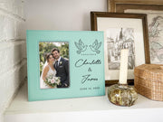 Edited mockup of a teal-toned Together frame beside a candle, with an illustrative wedding portrait at left and paired doves, Charlotte & James, and June 14, 2026 at right.