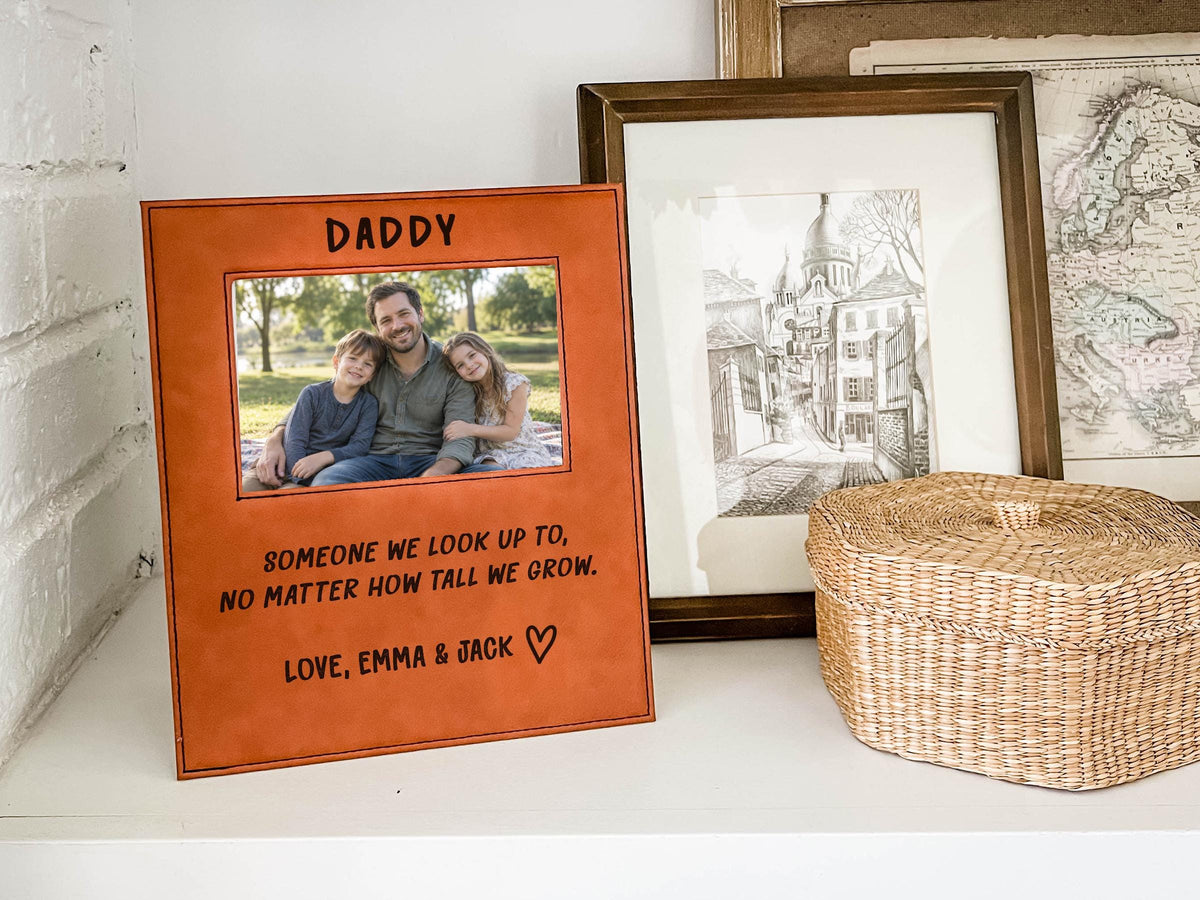 Edited mockup of the tall we grow Daddy frame beside a woven basket and framed art, with a sample dad-and-children photo, engraved saying, Love, Emma & Jack signature and outline heart.