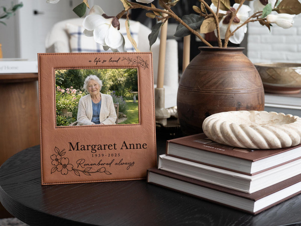 Edited memorial frame mockup beside books and a vase, with songbird and floral engraving, Margaret Anne, 1939-2025, and an illustrative portrait of an elderly woman.