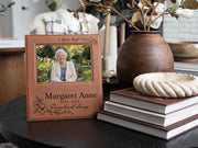 Edited memorial frame mockup beside books and a vase, with songbird and floral engraving, Margaret Anne, 1939-2025, and an illustrative portrait of an elderly woman.