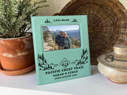 Edited mockup of the Pacific Crest Trail frame beside a plant and woven tray, with trail artwork, sample names and date, and an illustrative hiking couple photo.