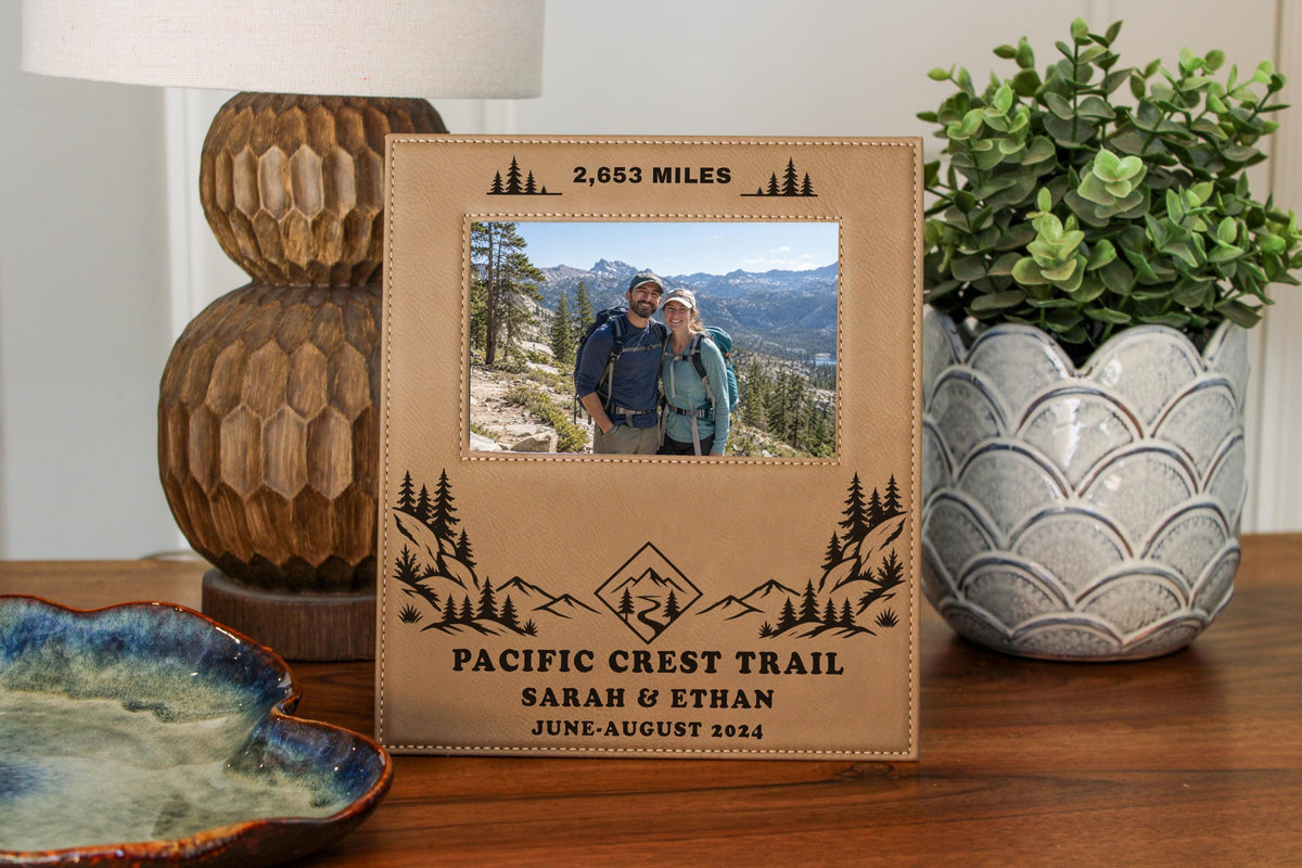 Edited mockup of the Pacific Crest Trail frame on a wooden table, showing sample mileage, names and date around an illustrative hiking couple photo.