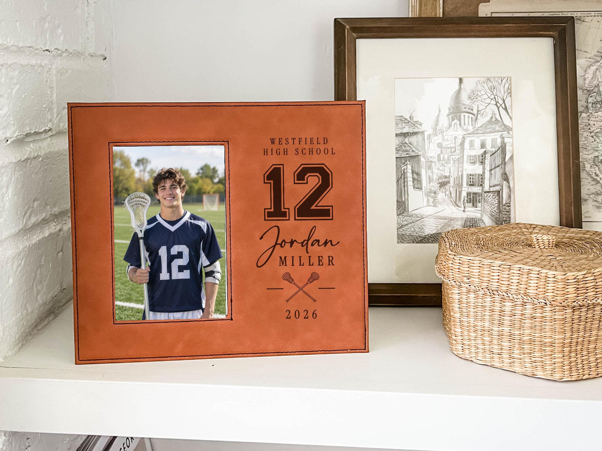 Varsity Lacrosse frame mockup on a white shelf beside framed art and a woven basket, with a lacrosse player portrait and personalized school, number, name and year.