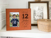 Varsity Lacrosse frame mockup on a white shelf beside framed art and a woven basket, with a lacrosse player portrait and personalized school, number, name and year.