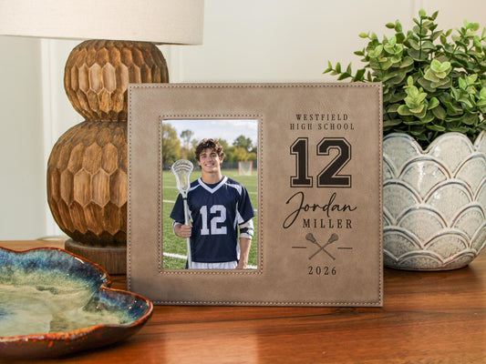 Varsity Lacrosse frame mockup beside a lamp and greenery, with a portrait of a lacrosse player and Westfield High School, number 12, Jordan Miller and 2026 engraving.