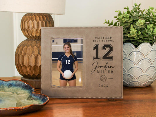 Edited Varsity Volleyball frame mockup beside a lamp and plant, with an illustrative athlete portrait on the left and Westfield High School, number 12, Jordan Miller and 2026 on the right.