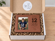 Varsity Football frame mockup in an open gift box with crinkle paper, a sample football player portrait, and personalized school, number, name, and year artwork.