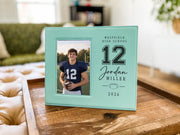 Teal Varsity Football frame mockup on a wooden tray, with a sample football player portrait on the left and school, number, name, football, and year on the right.
