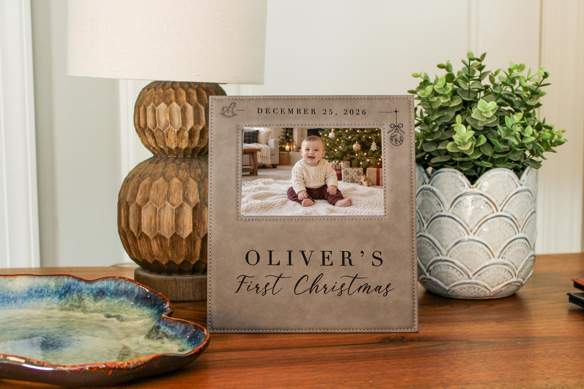 Edited mockup of Xmas Rocking Horse frame on a wooden tabletop between a lamp and plant, showing an illustrative baby photograph and personalized first Christmas engraving.