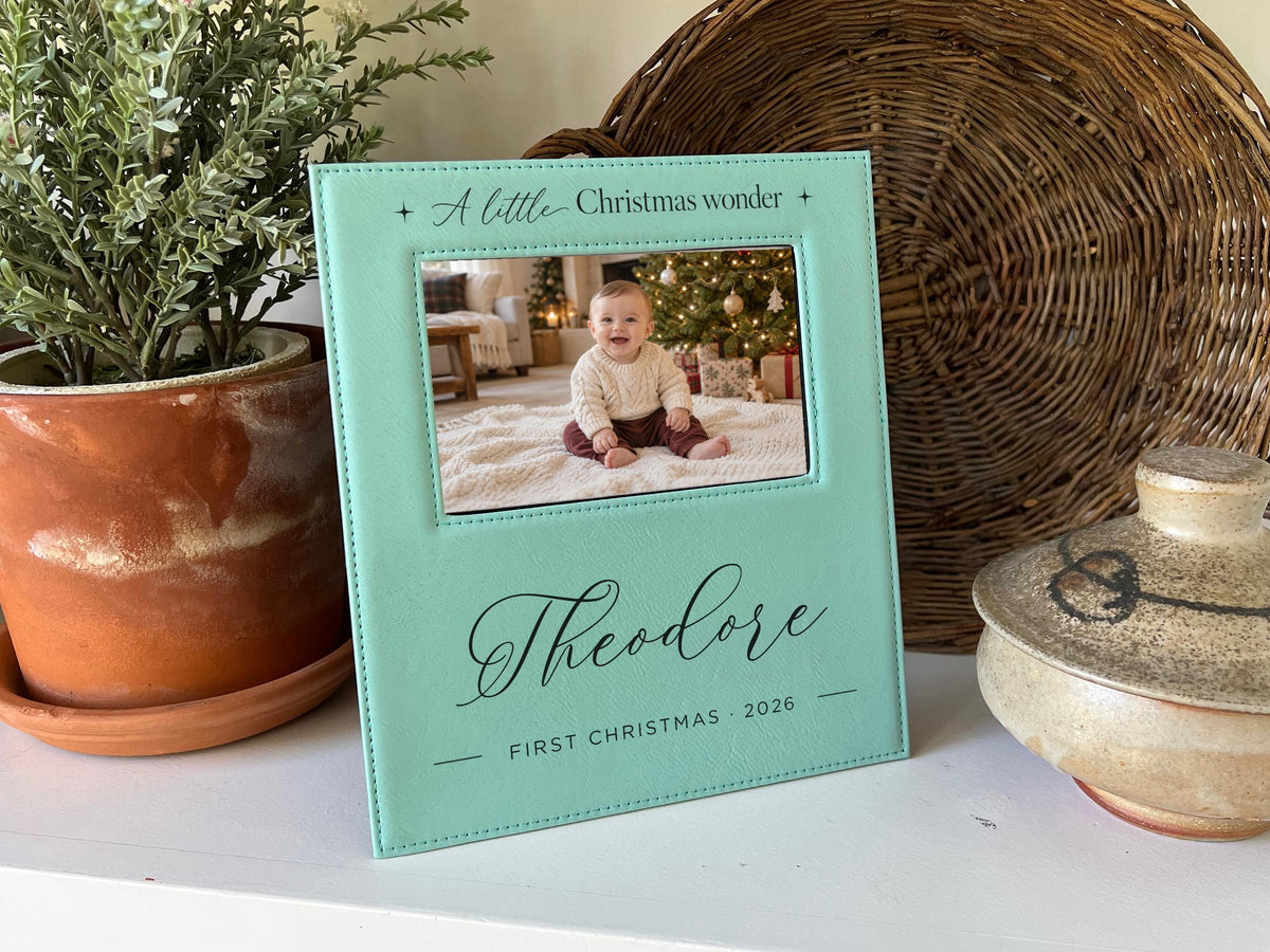 Edited mockup of Christmas Wonder frame with Theodore, First Christmas 2026 and an illustrative baby photograph, beside greenery and a woven tray.