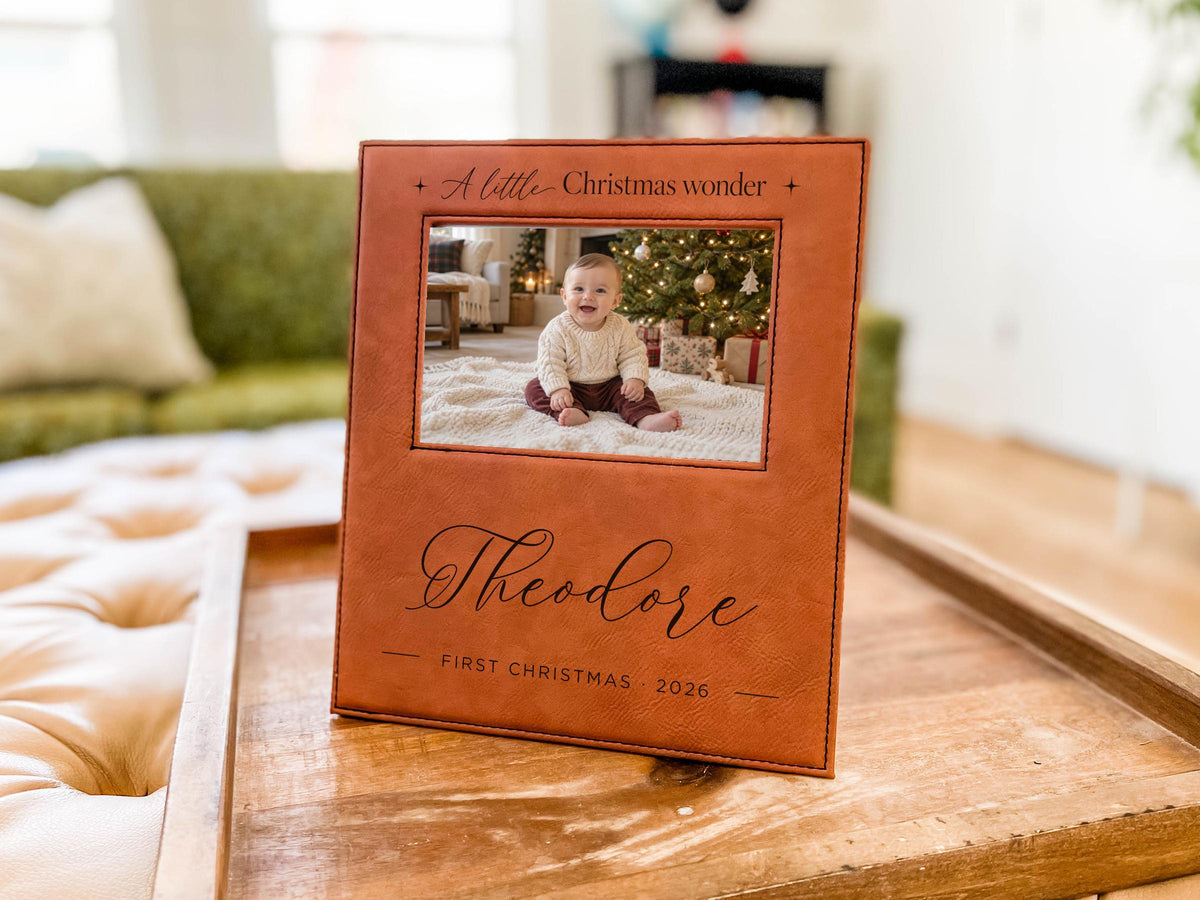 Edited mockup of Christmas Wonder frame engraved with Theodore and First Christmas 2026 around an illustrative baby photo, standing on a tray.