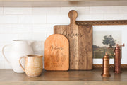 Kitchen Garden Trio personalized cutting board with three botanical herb sprigs and sample name wording; edited mockup.