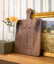 Kitchen Garden Trio personalized cutting board with three botanical herb sprigs and sample name wording; edited mockup.