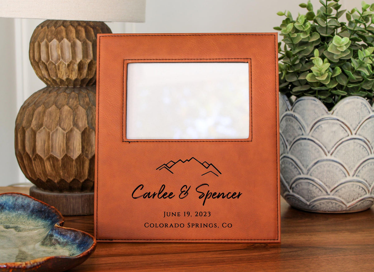 a wooden picture frame with a mountain design, placed on a wooden surface next to a potted plant and a decorative vase.