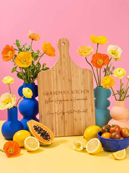 Grandma’s Kitchen bamboo paddle board engraved with grandchildren’s names, surrounded by colorful flowers.